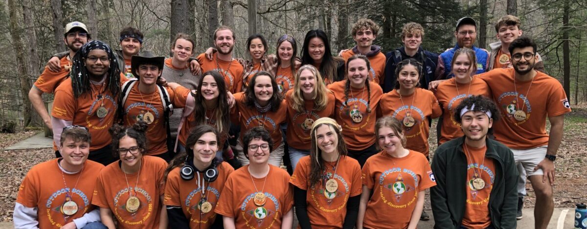 Outdoor School counselors pose for a group photo wearing matching orange t-shirts.
