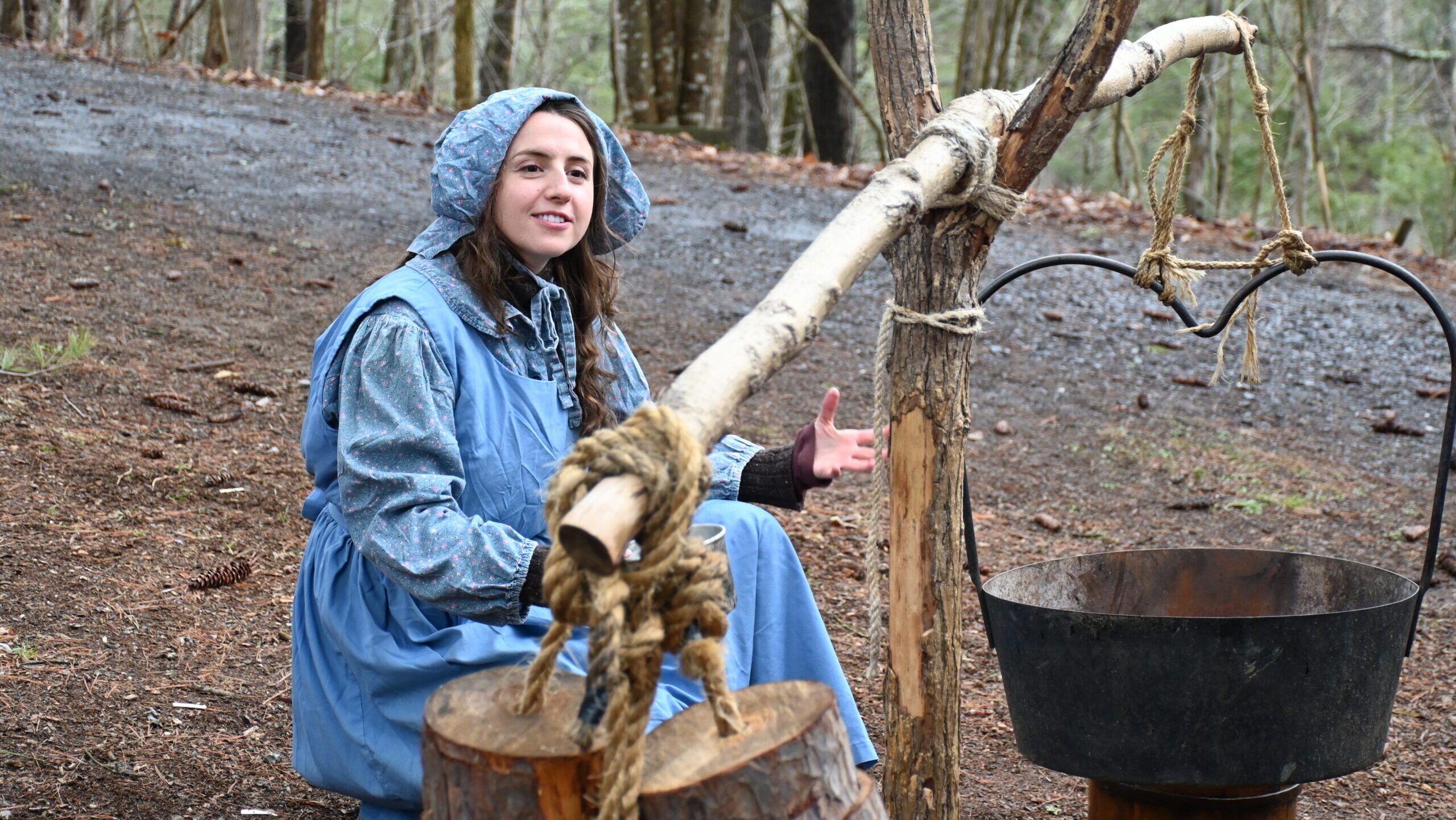 A student is dressed in a historical outfit and demonstrating the process of boiling sap to make maple syrup