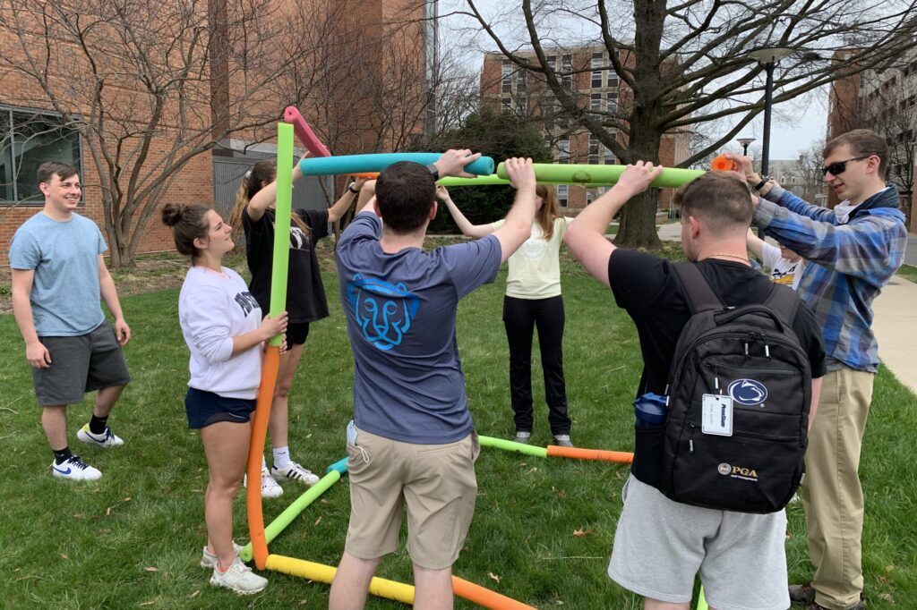 A group of students hold pool floats as they work on a team building puzzle.