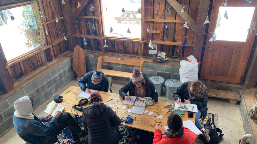 A group of people sketch twigs while sitting at a table in a pavilion